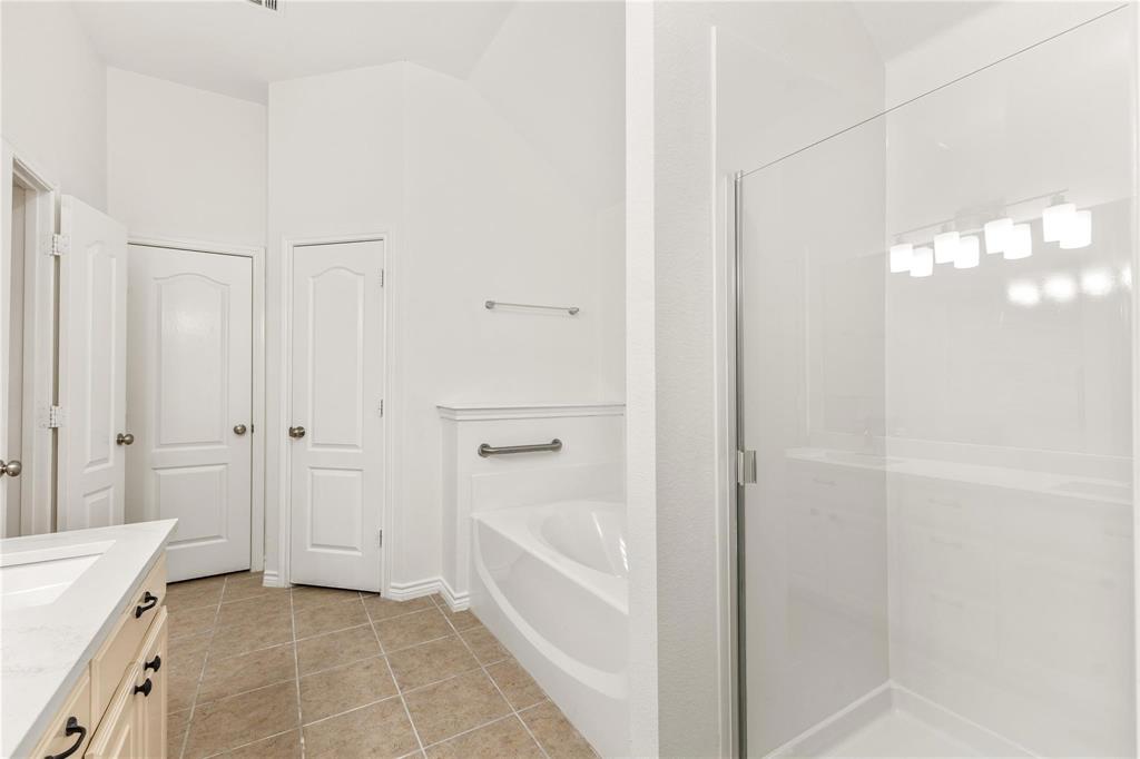 Bathroom featuring a built-in soaking tub, separate glass-enclosed shower, neutral-tone tile flooring, and light-toned cabinetry with a solid-surface countertop