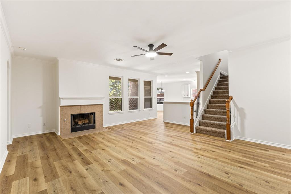 Open-concept area featuring wood-finish flooring, a fireplace with a stone-finish surround, triple-pane windows, a ceiling fan, and a staircase with a wood handrail