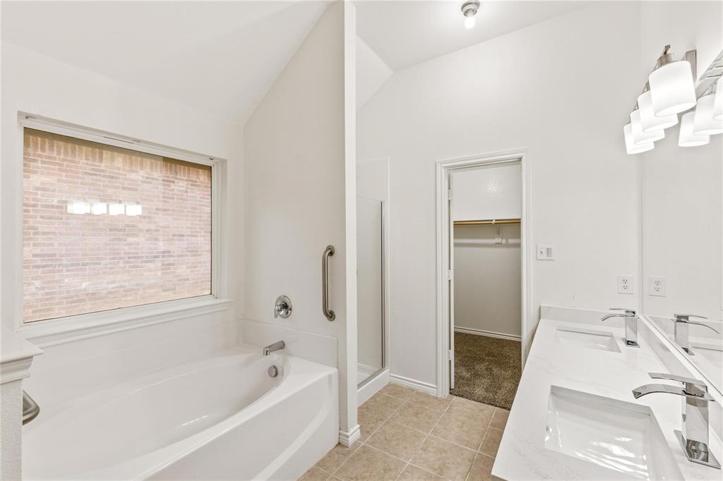 Dual-sink vanity with white countertops and polished chrome faucets, soaking tub, glass-enclosed shower, and built-in closet shelving