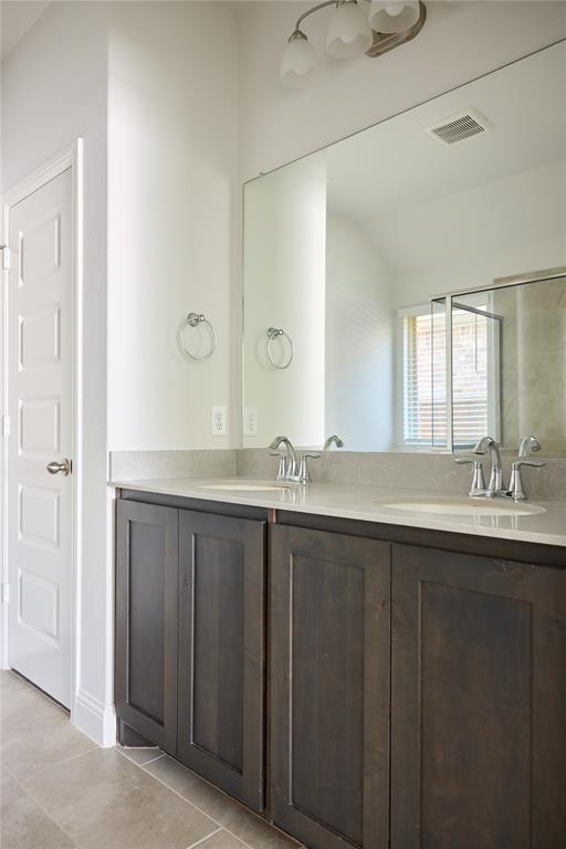 Double vanity featuring dark-stained wood cabinetry, stone-finish countertops, dual undermount sinks, and a full-width wall mirror