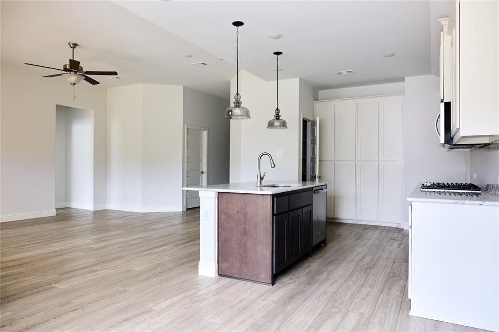 Kitchen featuring a center island with a stone countertop, built-in cabinetry, wood-finish flooring, dual pendant lighting, and a stainless steel sink fixture