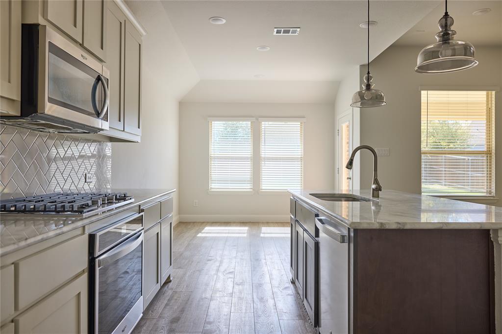 Kitchen featuring stone countertops, a center island with undermount sink, herringbone-patterned tile backsplash, stainless steel appliances, and wood-finish flooring