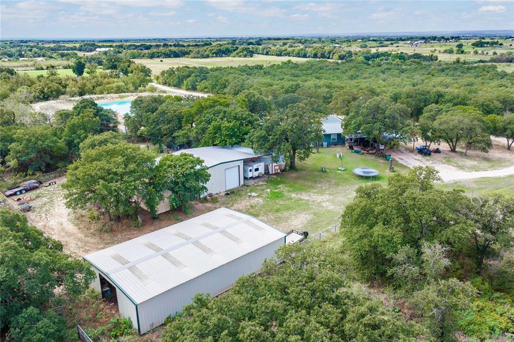 Expansive rural acreage featuring two detached metal-sided workshops, mature tree canopy, and gravel driveways
