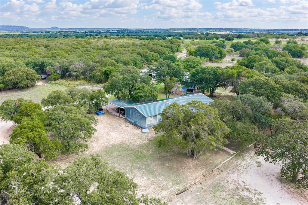 Residential property featuring a metal roof, an attached carport, and extensive surrounding acreage with mature trees