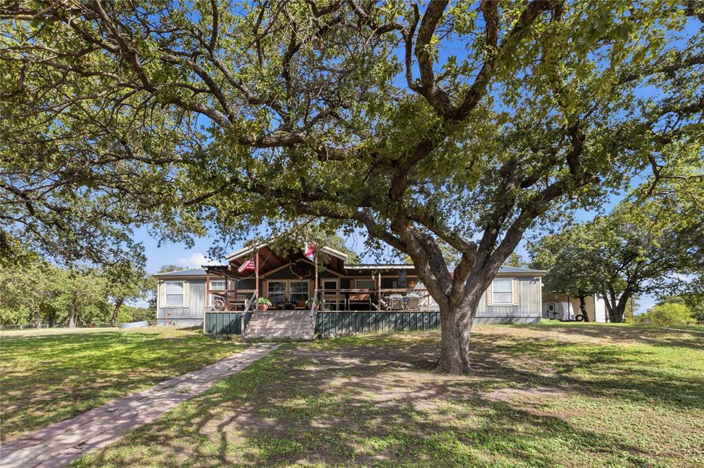 Exterior facade featuring a covered front porch, metal roofing, mature oak trees, and a stone walkway