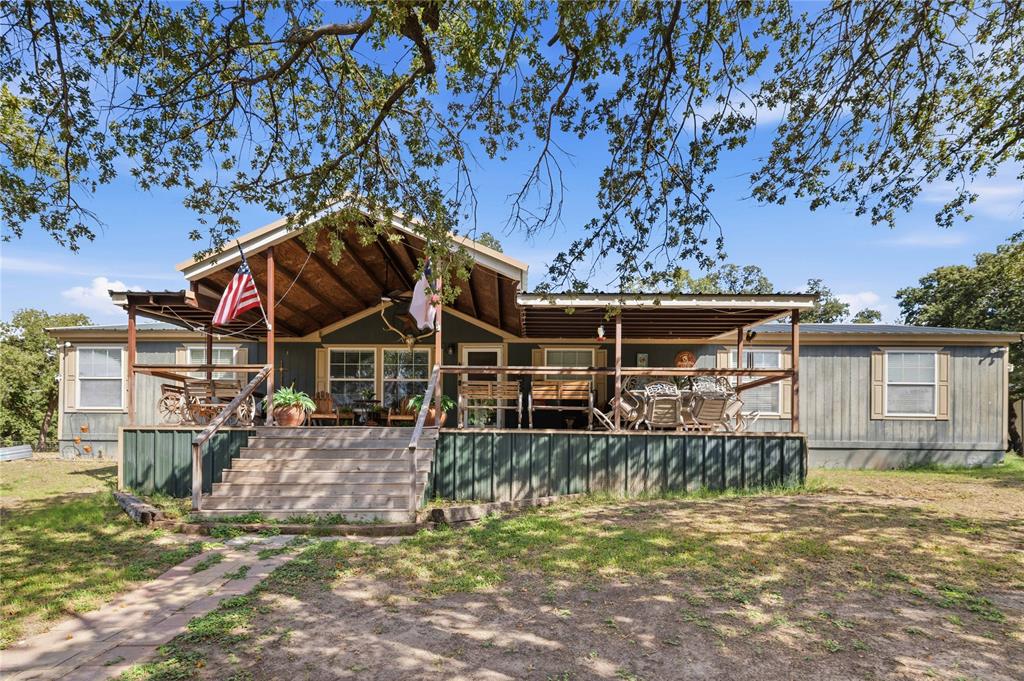 Single-story residence featuring a wood-siding exterior, expansive front deck, gabled roofline with exposed beam ceiling, and shutter-framed windows