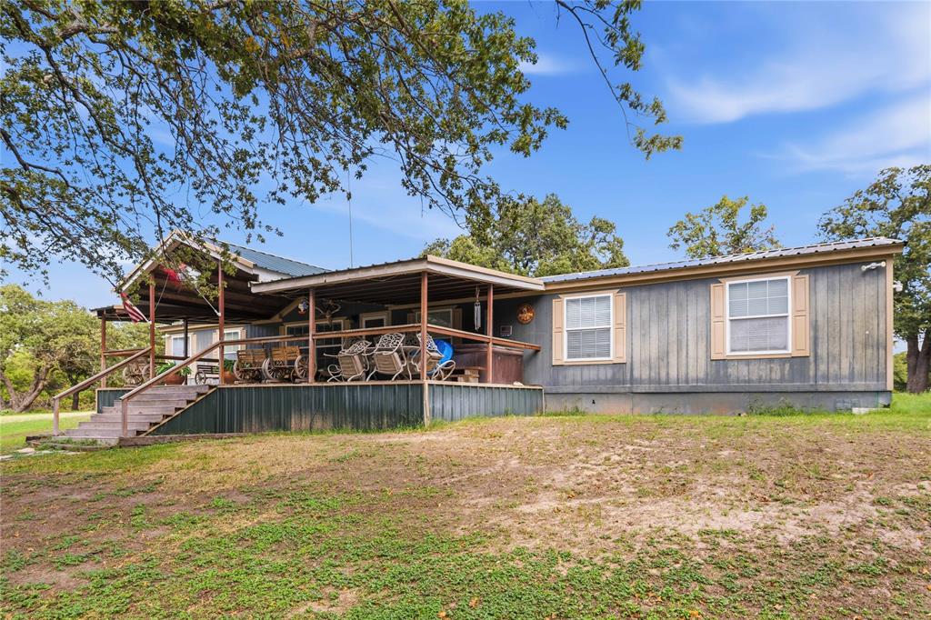 Exterior featuring vertical panel siding, a metal roof, and an expansive covered porch with wooden stairs and railing