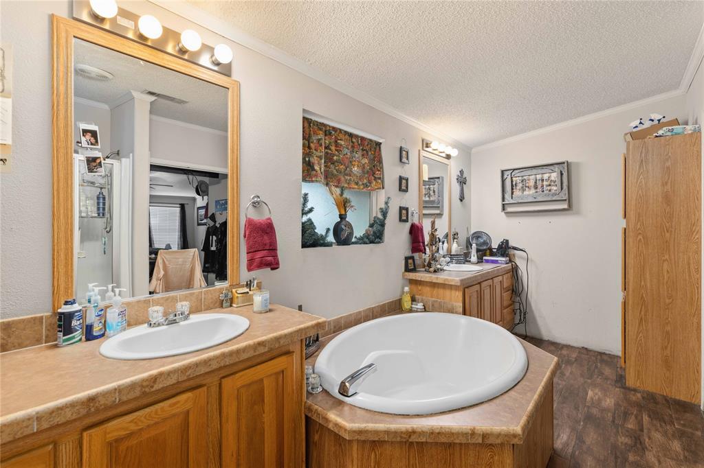 Bathroom featuring dual wood-finish cabinetry, tile-surround drop-in soaking tub, wood-finish flooring, and wall-mounted vanity lighting