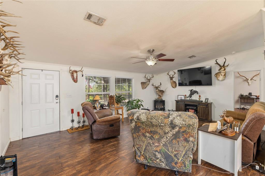 Living area featuring wood-finish flooring, white panel door, multi-pane windows, and a ceiling fan with integrated lighting