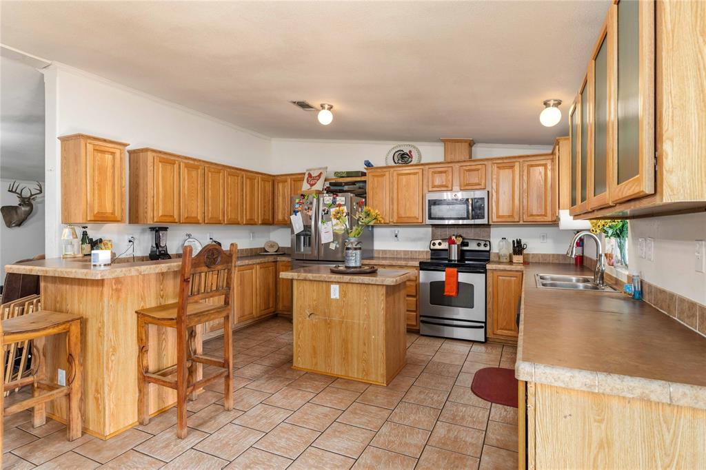 Kitchen featuring light-finish wood cabinetry, a central island, stainless steel appliances, ceramic tile flooring, and a breakfast bar