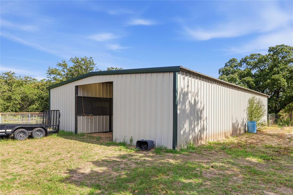 Metal-sided agricultural structure featuring a covered stall, corrugated metal siding, and a low-pitch roof