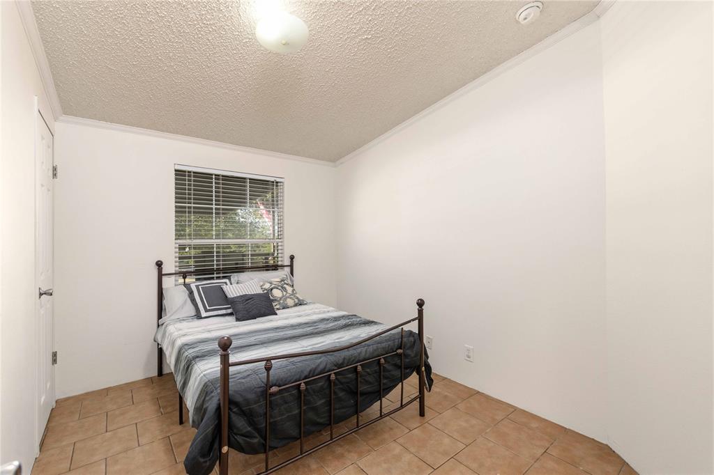 Room with neutral walls, tiled flooring, textured ceiling, and a window fitted with horizontal blinds