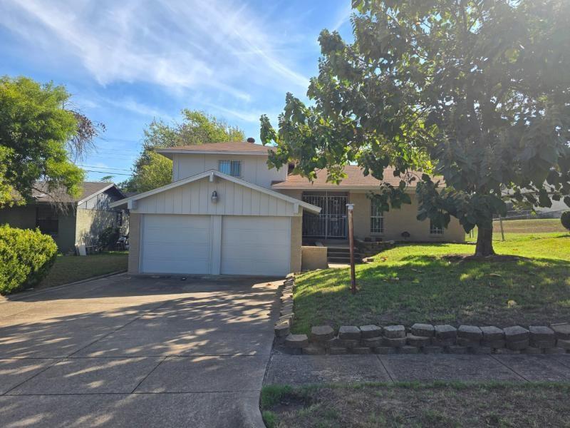 Two-story exterior featuring a double-car garage, shingled roof, concrete driveway, and stone-block landscaping border Two-story exterior featuring a double-car garage, shingled roof, concrete driveway, and stone-block landscaping border