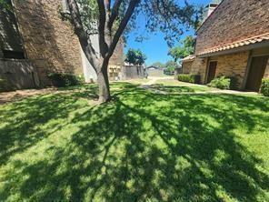 Exterior courtyard featuring brick masonry, a central mature tree, a manicured lawn, and a paved walkway