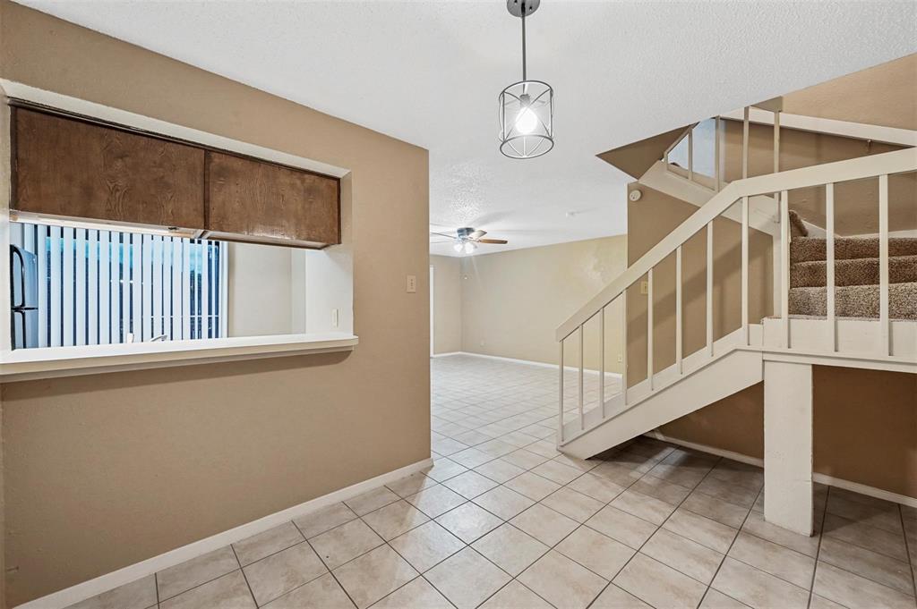 Interior area featuring ceramic tile flooring, a pass-through window with built-in wooden cabinetry, a geometric pendant light fixture, and a staircase with a white wooden railing