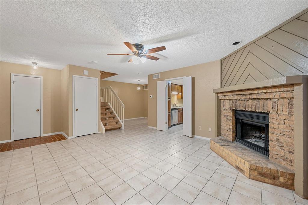 Interior area featuring tile flooring, a floor-to-ceiling brick fireplace with an elevated hearth, a decorative wood-panel accent wall, and a staircase with a wooden balustrade