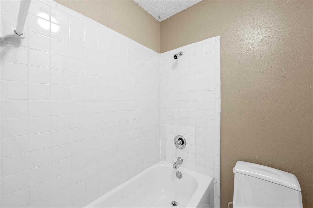 Bathtub with white tiled surround, chrome shower head and faucet hardware, and standard toilet