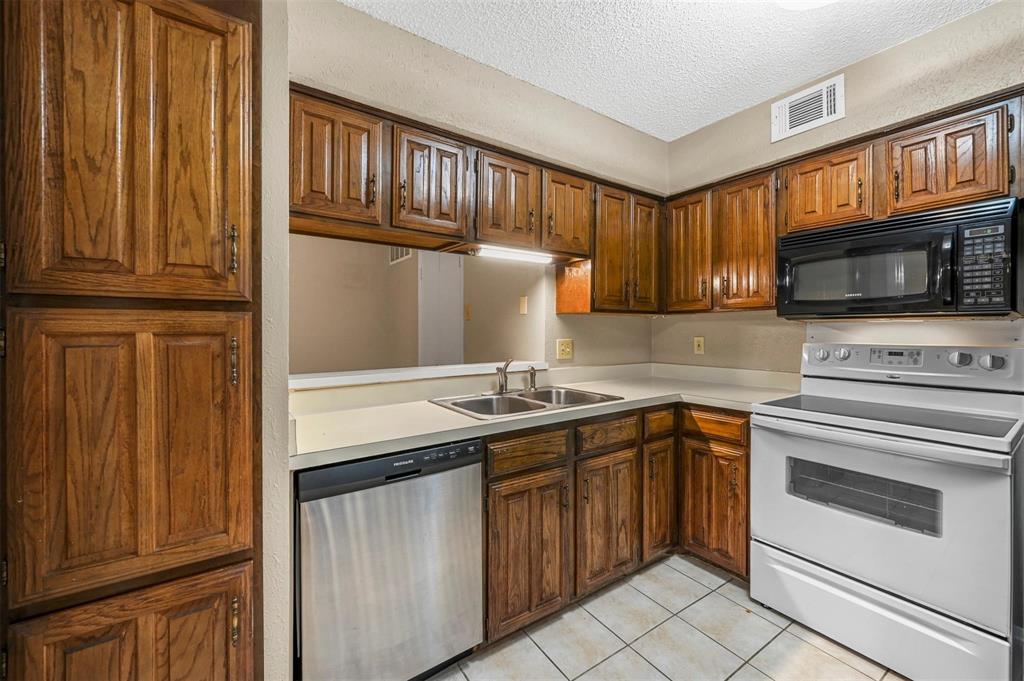 Kitchen featuring stained wood cabinetry, solid-surface countertops, stainless steel dishwasher, built-in microwave, and tile flooring