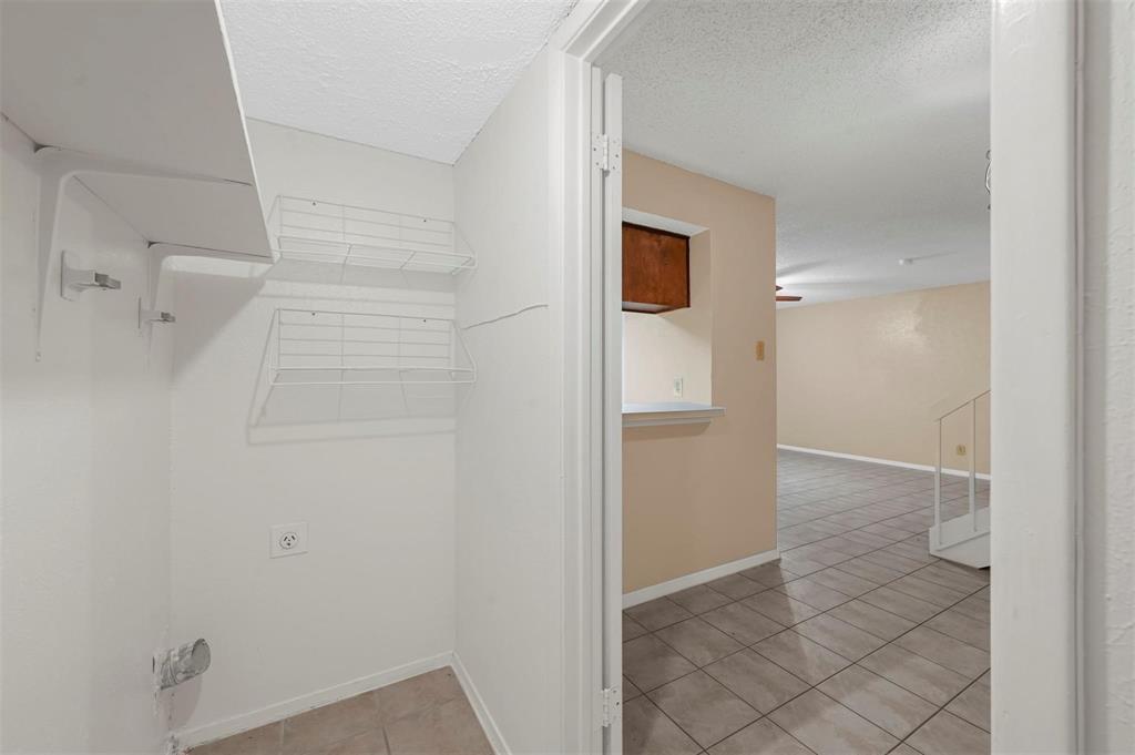 Utility space featuring wall-mounted wire shelving, tile flooring, and dedicated electrical and plumbing connections
