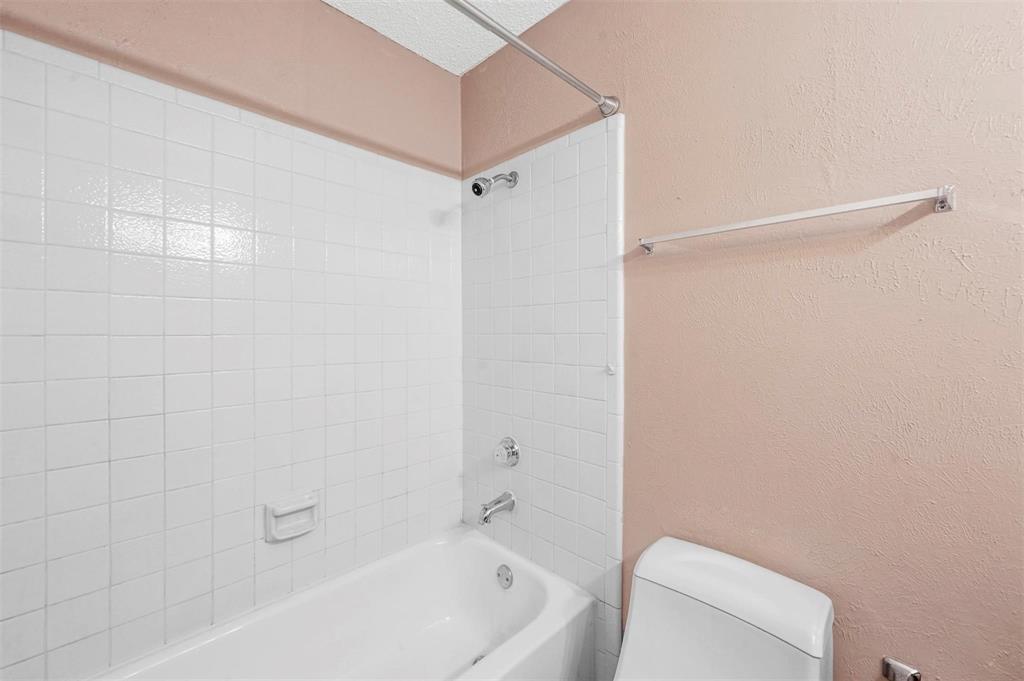 Bathtub enclosure featuring white square tile wall surrounds, a built-in recessed soap niche, chrome plumbing fixtures, a metal curtain rod, and a wall-mounted towel bar