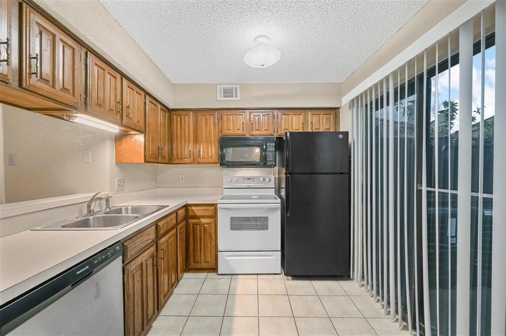 Kitchen featuring wood cabinetry, ceramic tile flooring, solid-surface countertops, dual-basin stainless steel sink, and sliding glass patio door