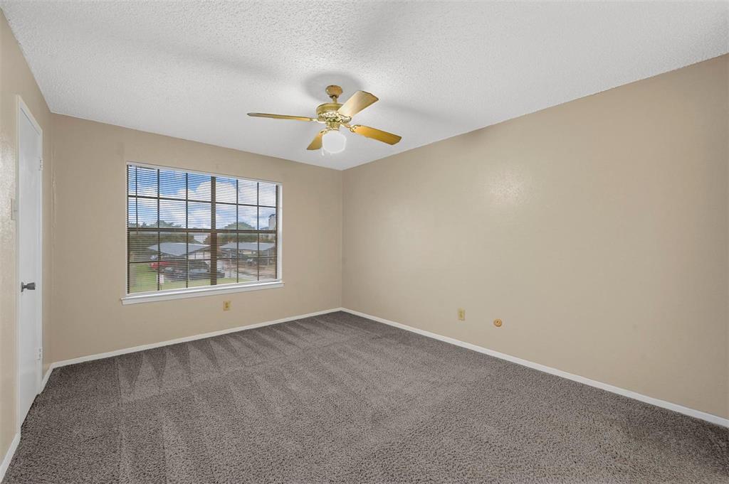 Neutral-toned interior space featuring wall-to-wall carpeting, multi-pane window, and a ceiling fan with integrated light fixture