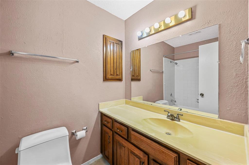 Bathroom featuring a vanity with integrated sink, wood-finish cabinetry, a large wall-mounted mirror, overhead five-bulb lighting, and a white tiled shower surround
