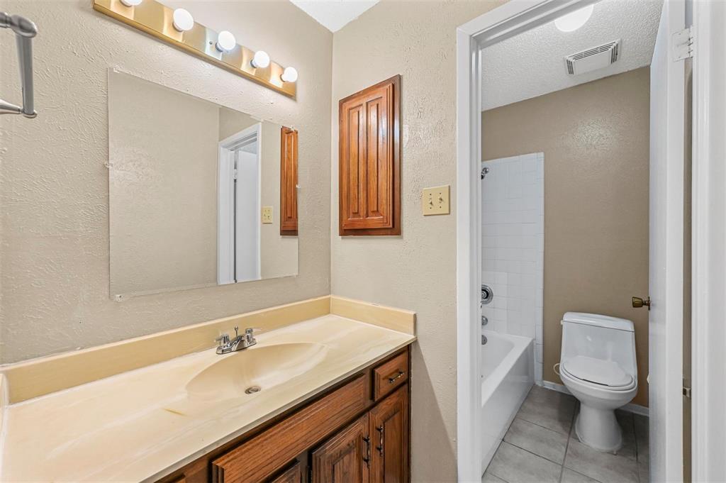 Bathroom featuring a vanity with an integrated basin, wood-tone cabinetry, wall-mounted medicine cabinet, four-bulb vanity light, and a tub-shower combination with tile surround