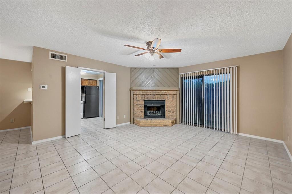 Corner fireplace featuring brick masonry and a raised hearth, tile flooring, ceiling fan, and sliding glass doors
