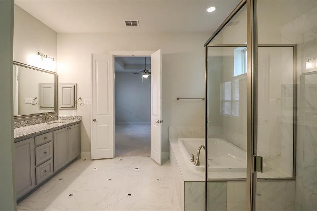 Bathroom featuring a vanity with stone-finish countertop, undermount sink, built-in soaking tub, separate glass-enclosed shower, and large-format tile flooring with decorative inserts