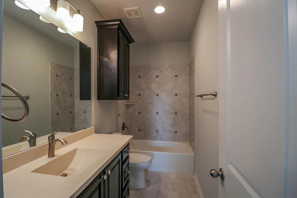 Bathroom featuring dark wood cabinetry, an integrated sink with a metallic faucet, a large vanity mirror, and a tiled tub surround with decorative inserts