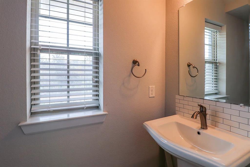 Pedestal sink with a metal faucet, subway tile backsplash, wall-mounted towel ring, and window with slat blinds