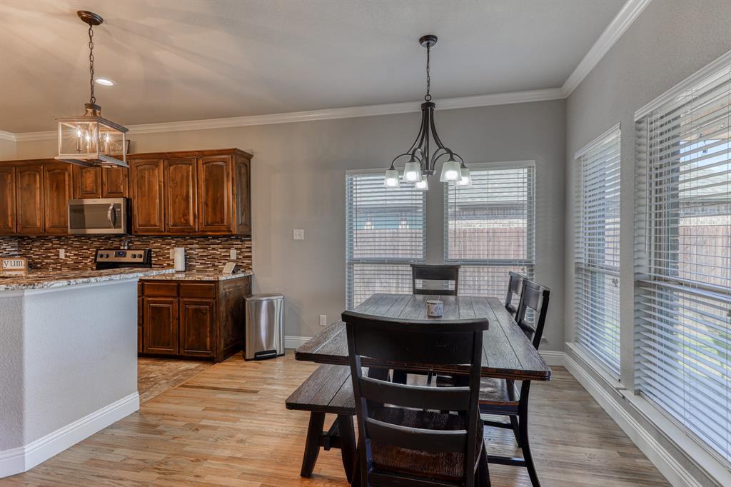 Kitchen featuring stained wood cabinetry, stone-patterned backsplash, wood-finish flooring, crown molding, and two distinct overhead pendant light fixtures