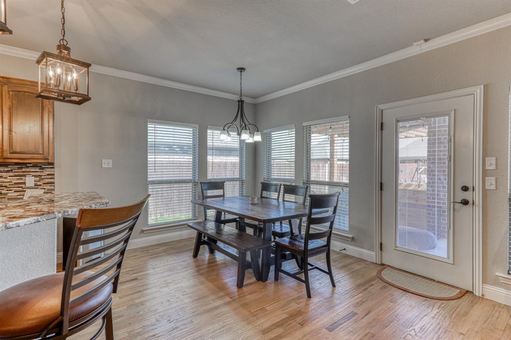 Dining area featuring wood-finish flooring, multi-pane windows with integrated blinds, crown molding, and a decorative pendant light fixture