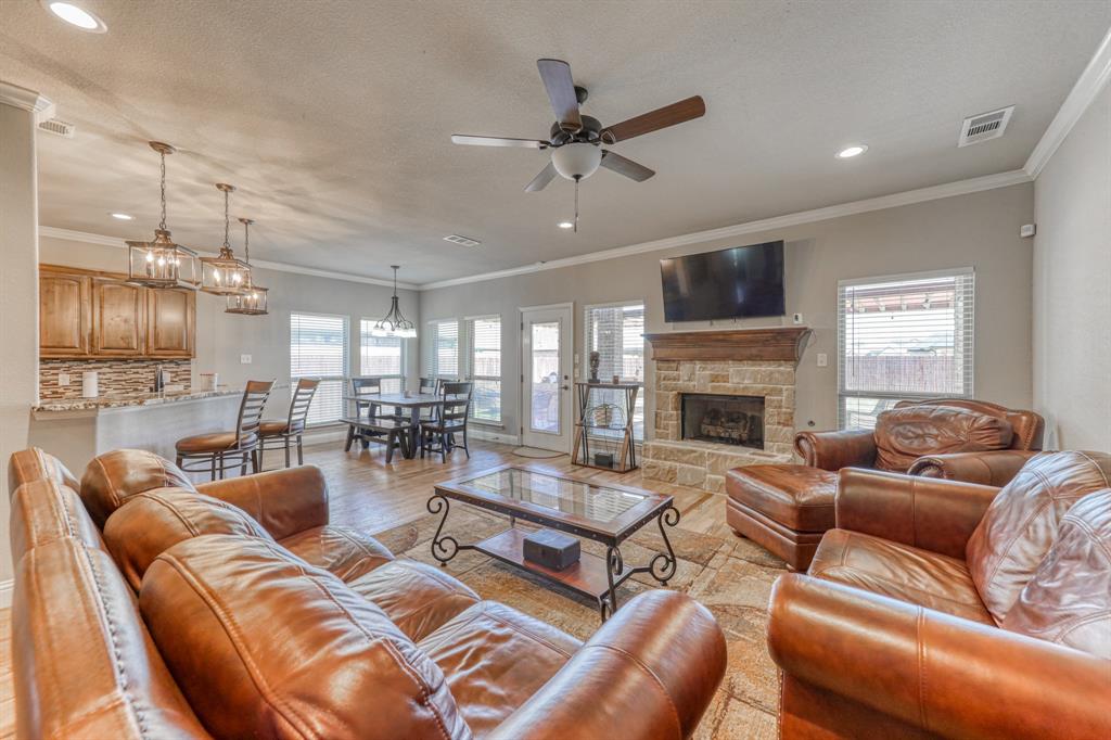 Open-concept living area featuring a stone-faced fireplace with a natural wood mantel, recessed lighting, ceiling fan, and tile flooring
