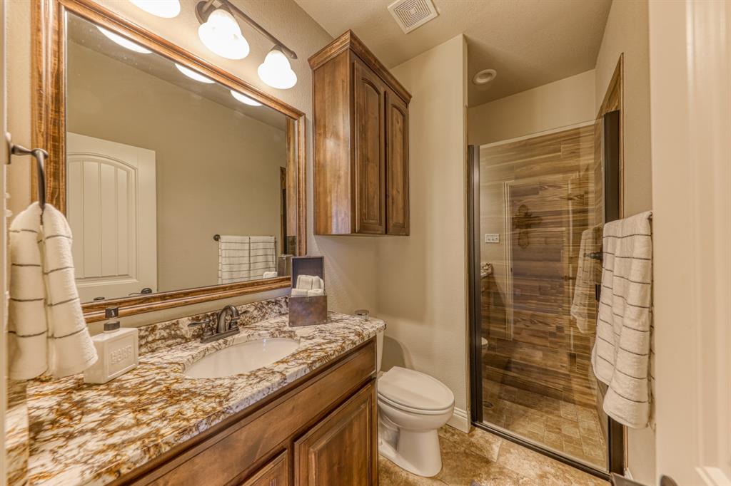 Bathroom featuring stone-finish countertop, dark wood-finish cabinetry, framed vanity mirror, and glass-enclosed shower with tile surround