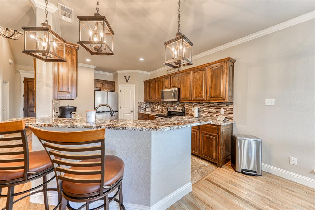 Kitchen featuring stained wood cabinetry, multi-tonal backsplash tile, stone-finish countertops, and hanging geometric lantern lighting