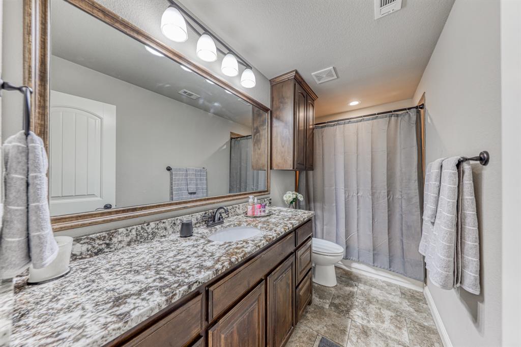 Bathroom featuring a stone-patterned countertop, dark wood-finish cabinetry, an expansive wall-mounted mirror, four-light vanity fixture, and tiled flooring