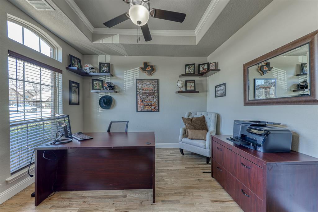 Tray ceiling with crown molding, wood-finish flooring, ceiling fan with integrated light fixture, large arched window, and wall-mounted floating shelves
