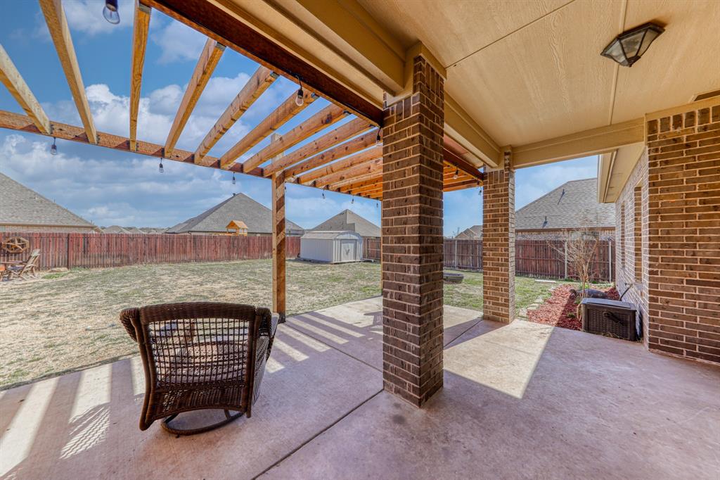 Covered concrete patio featuring a cedar pergola, brick structural pillars, and string lighting