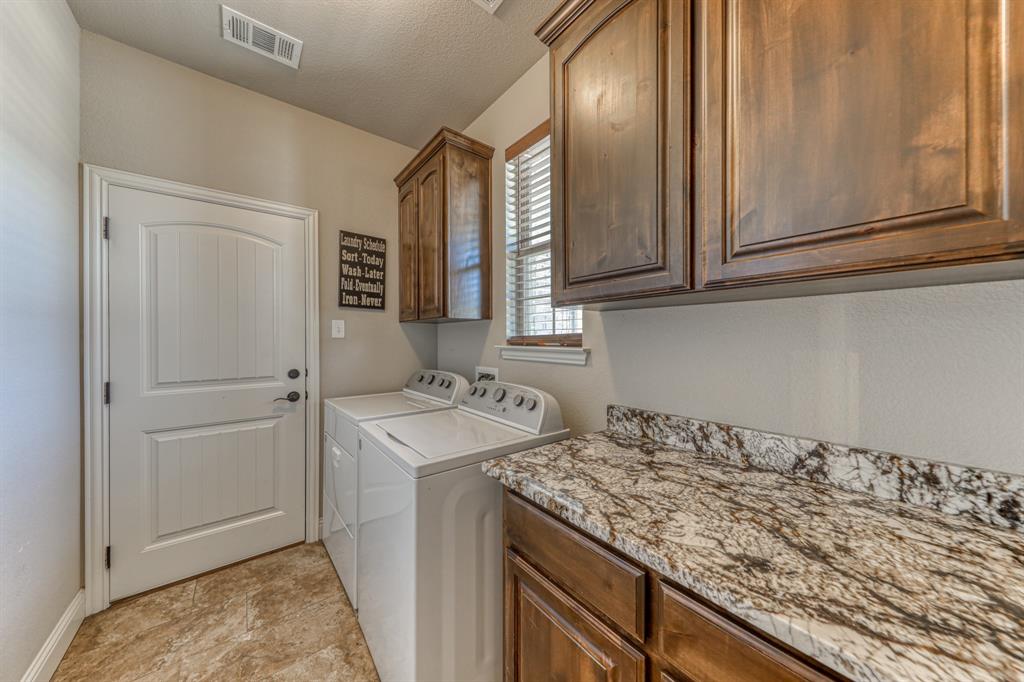 Laundry area featuring raised-panel wood cabinetry, natural stone countertops, tile flooring, and a single-panel interior door