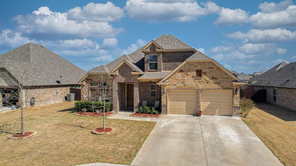 Multi-gabled brick and stone exterior featuring a two-car garage, steep shingled rooflines, and a concrete driveway