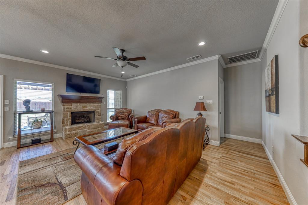 Living area featuring wood-finish flooring, a stone-faced fireplace with a timber mantel, crown molding, and recessed lighting