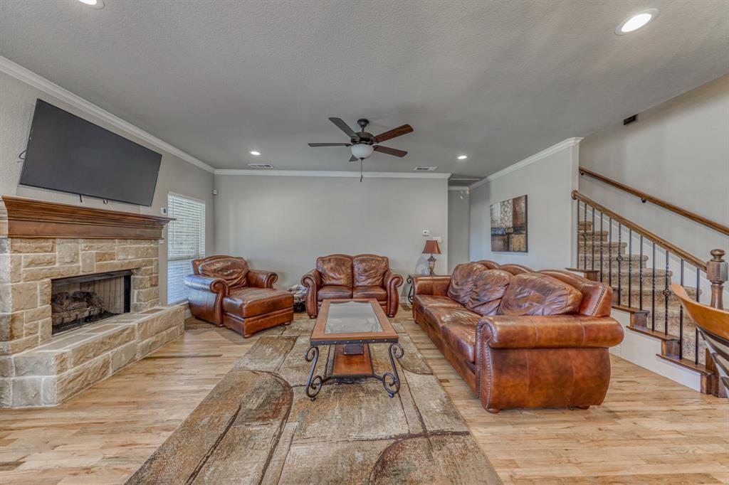 Stone-faced fireplace with a wood mantel, wood-finish flooring, recessed lighting, ceiling fan, and staircase with a wood handrail and metal balusters