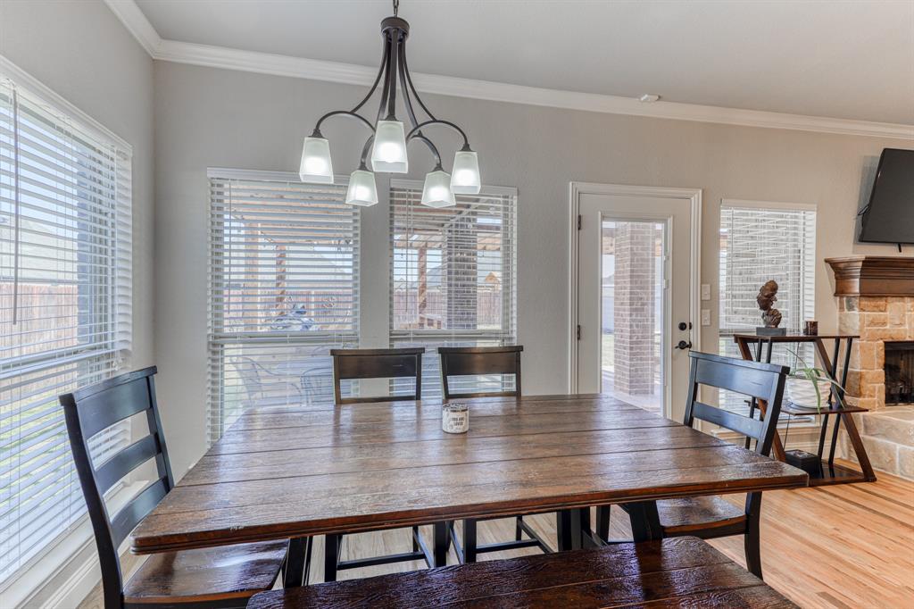 Dining area featuring multi-light metal chandelier, windows with horizontal blinds, glass-panel exterior door, and stone-surround fireplace with wood mantel