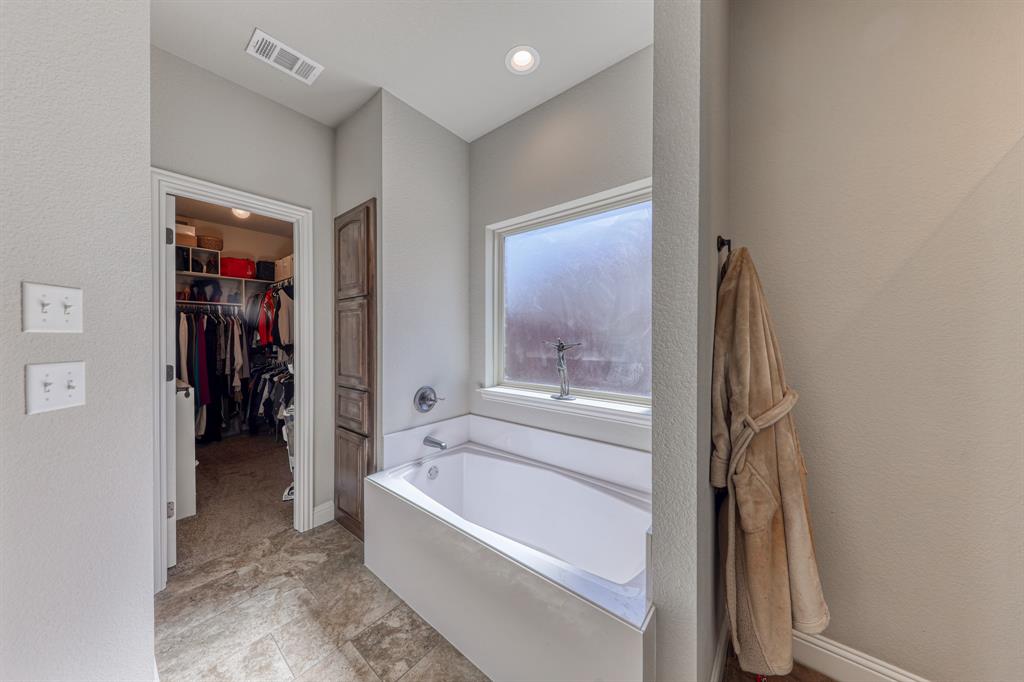 Deep soaking tub with a metal faucet, tile flooring, built-in wooden cabinetry, recessed ceiling lighting, and a privacy window