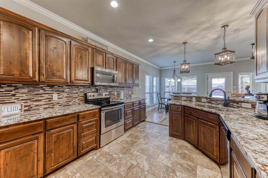 Kitchen featuring stained wood cabinetry, patterned stone-surface countertops, horizontal multi-tone tile backsplash, stainless steel appliances, and tile flooring