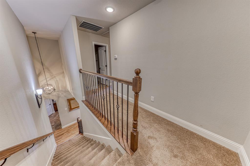 Carpeted hallway featuring a wood and metal balustrade, recessed ceiling lighting, and a multi-light spherical chandelier