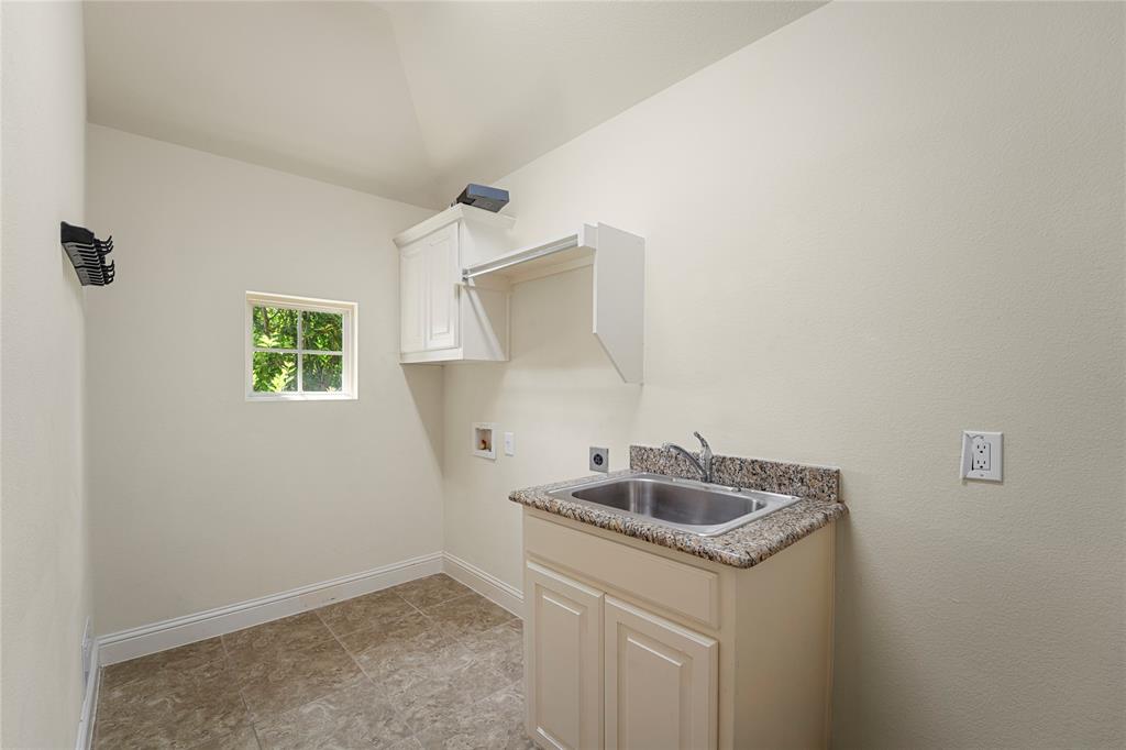 Utility room featuring stone-finish countertop with drop-in stainless steel sink, built-in cabinetry, overhead shelving, and tile flooring