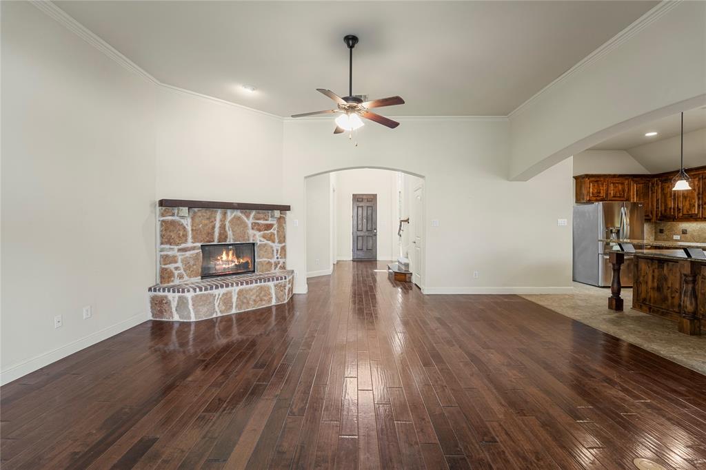 Living area featuring wood-finish flooring, a corner masonry fireplace with a wood mantel, an arched entry, and a ceiling fan